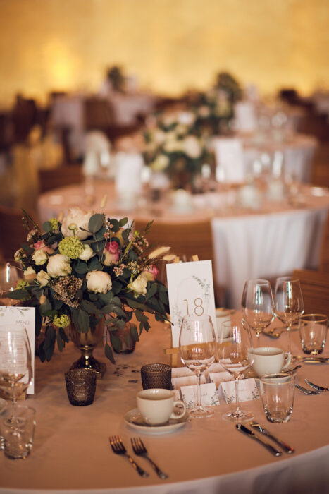 Festlich gedeckter Tisch mit Blumenarrangement, Tischkarten und Gläsern, warme Beleuchtung, Hochzeit oder Gala-Veranstaltung