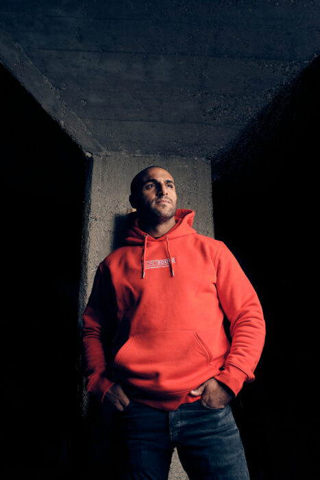 Portrait eines Mannes im roten Hoodie in urbaner Architektur mit hartem Licht